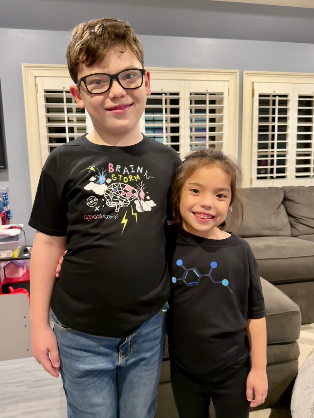 Ladyspinedoc's son wearing the Ladyspinedoc x The Neuron Family - Youth Brain Storm Tee Shirt in Black. Next to him is Ladyspinedoc's daughter wearing the Dr. Beachgem Code Cart Youth tee shirt in black. 