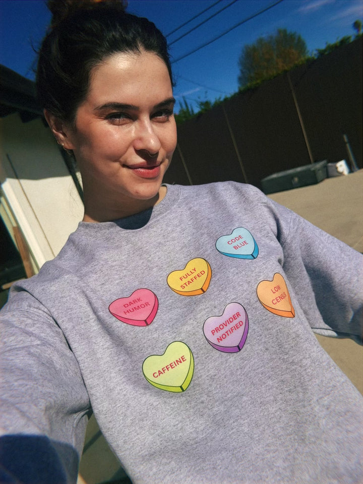 Scrubhacks outside wearing a gray sweatshirt with colorful candy hearts with medical lingo in each