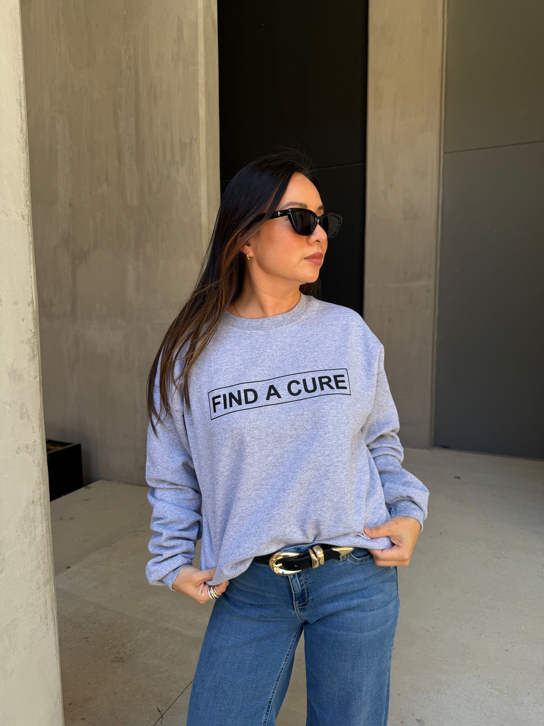 Person wearing a gray sweatshirt with 'Find a Cure' text, standing against a neutral wall.