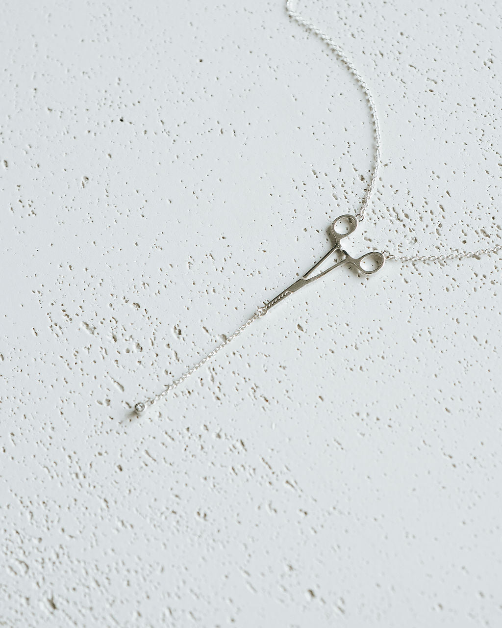 Flat lay of silver Erin Necklace: Hemostat With Diamond Drop