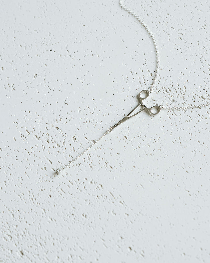 Flat lay of silver Erin Necklace: Hemostat With Diamond Drop