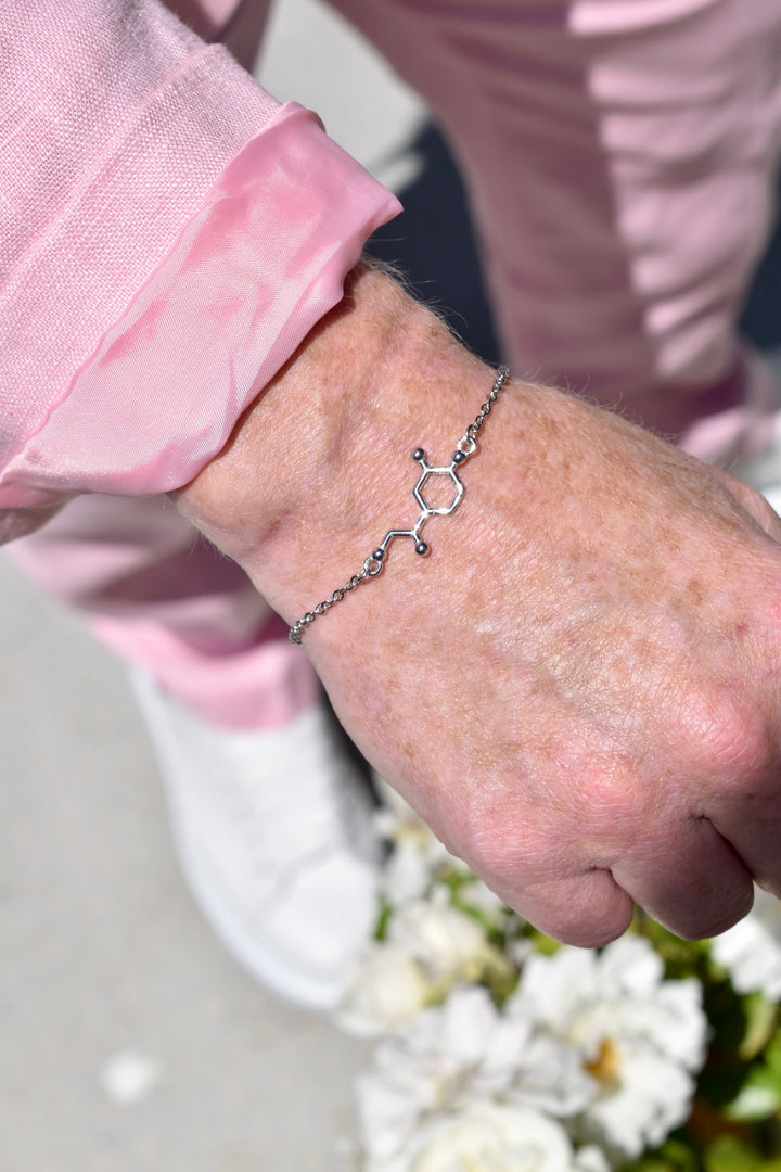 Close-up of a Ladyspinedoc's hand wearing a silver Dr. Beachgem bracelet with a noradrenaline molecular design, against a blurred background.