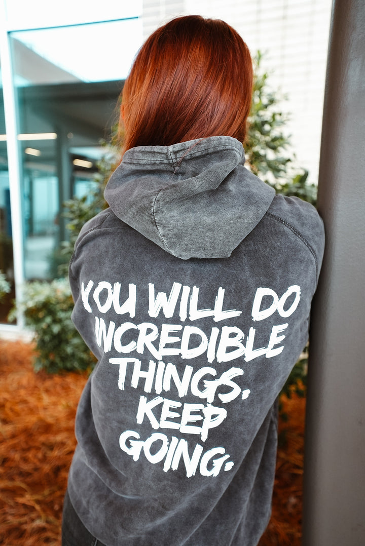 Dr. Betsy Grunch (Ladyspinedoc) wearing the Incredible Hoodie, displaying the back of the shirt showing bold white brushstroke message: “YOU WILL DO INCREDIBLE THINGS. KEEP GOING.”
