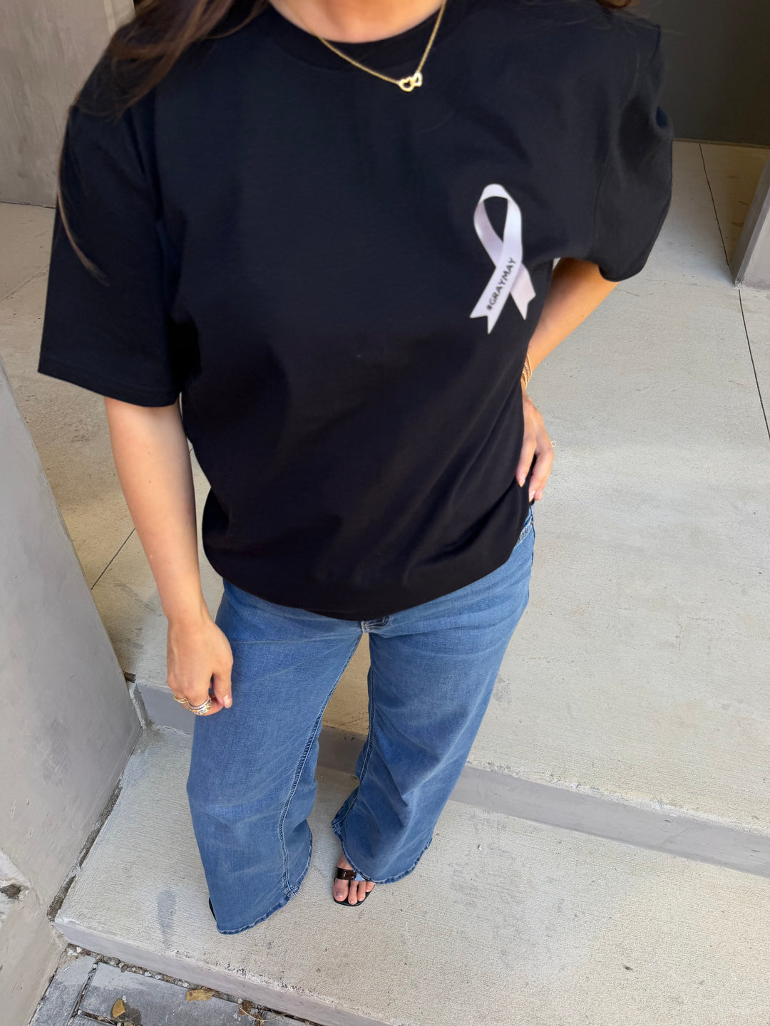Person wearing a black shirt with a gray ribbon logo and blue jeans.