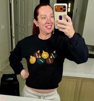 Ladyspinedoc wearing a black cropped surgical ornament sweatshirt, and taking a mirror selfie.