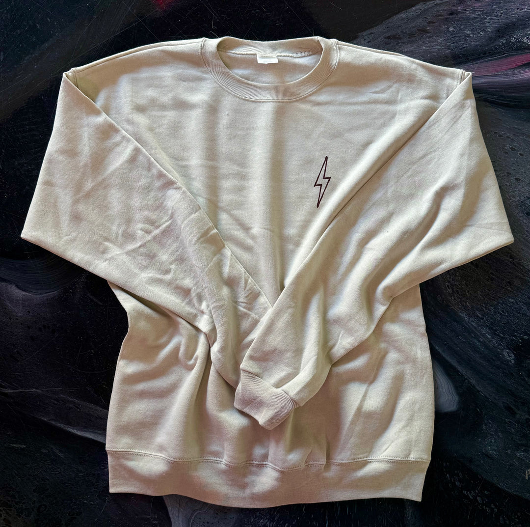 Front of sand-colored Increcible sweatshirt with a brown lightning bolt design on a dark background