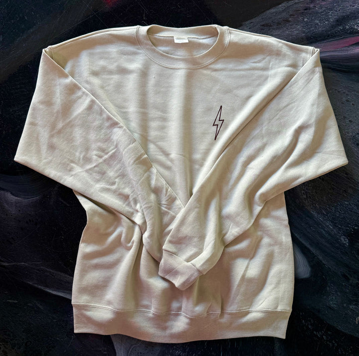 Front of sand-colored Increcible sweatshirt with a brown lightning bolt design on a dark background