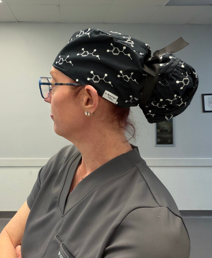 Ladyspinedoc wearing a black scrub cap with molecular designs and gray scrubs in an indoor setting.