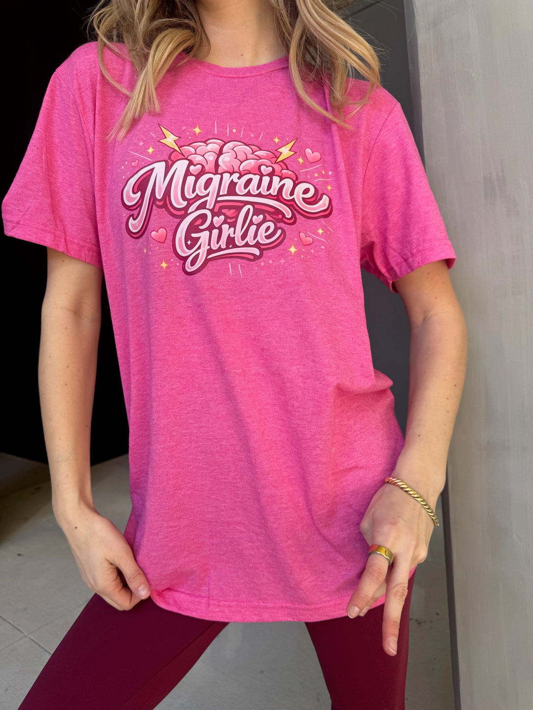 Person wearing a pink t-shirt with 'Migraine Girlie' text
