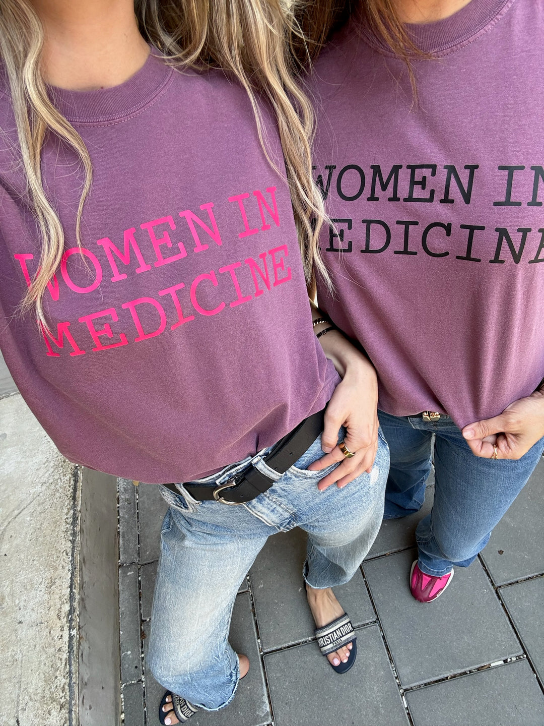 Two people wearing purple 'Women in Medicine' t-shirts on a sidewalk.