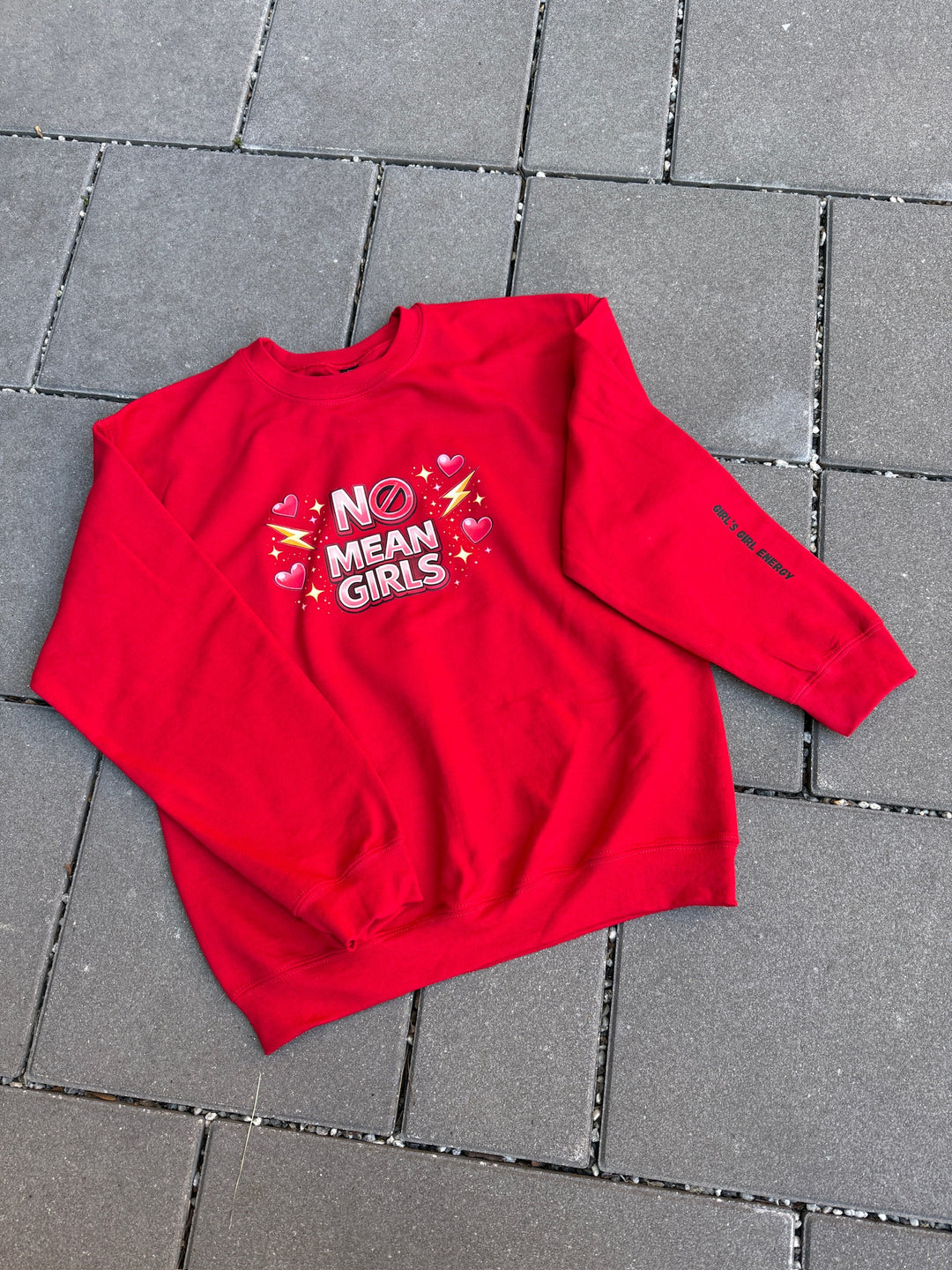 Red sweatshirt with 'No Mean Girls' text and 'Girl's Girl Energy' sleeve art on a tiled floor