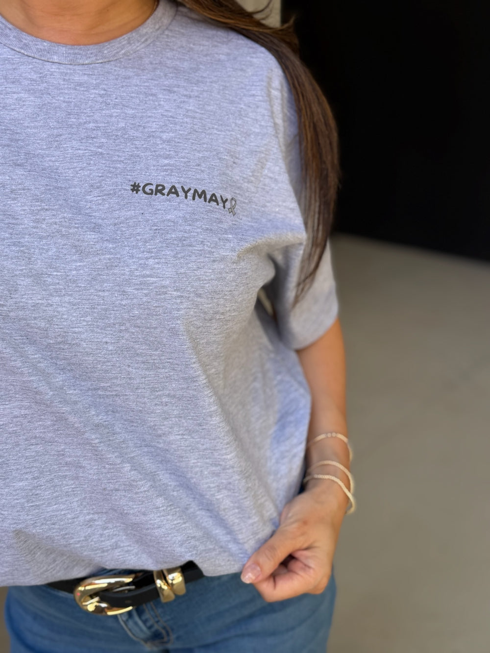 Person wearing a gray t-shirt with '#GRAYMAY' logo, holding a phone.