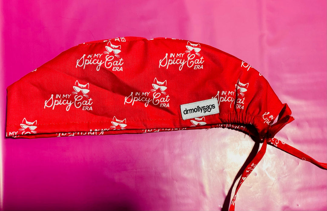 Red scrub cap with 'My Spicy Cat Era' text and logo on a pink background