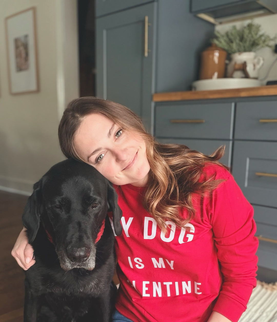 Dr Molly in a red My Dog Is My Valentine long sleeve shirt with a black dog in a kitchen setting