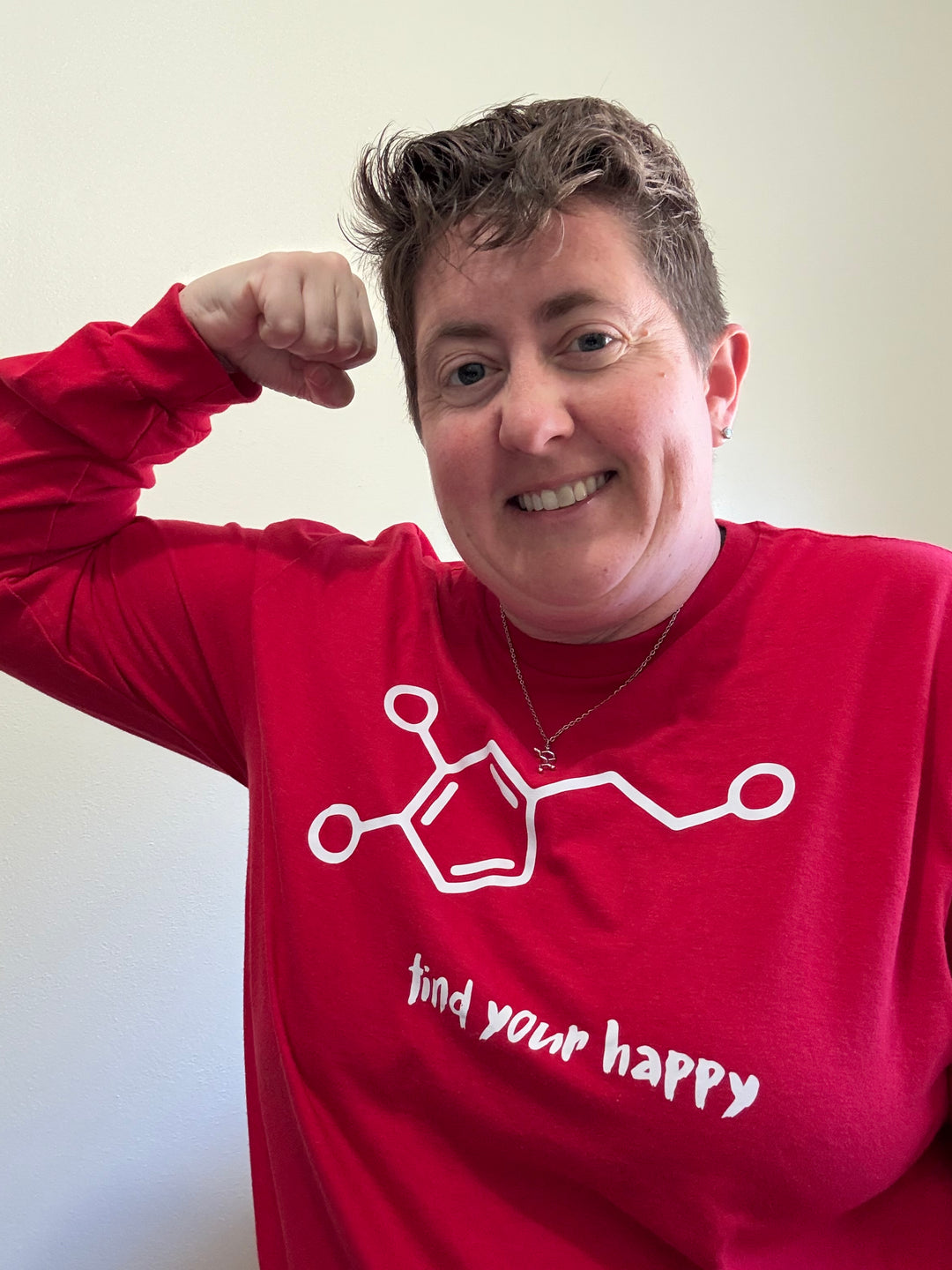 Dr. Beachgem doing a strong arm and wearing a red sweatshirt featuring a white dopamine molecule with “find your happy” printed in lowercase white letters in a cheerful brush font underneath. 
