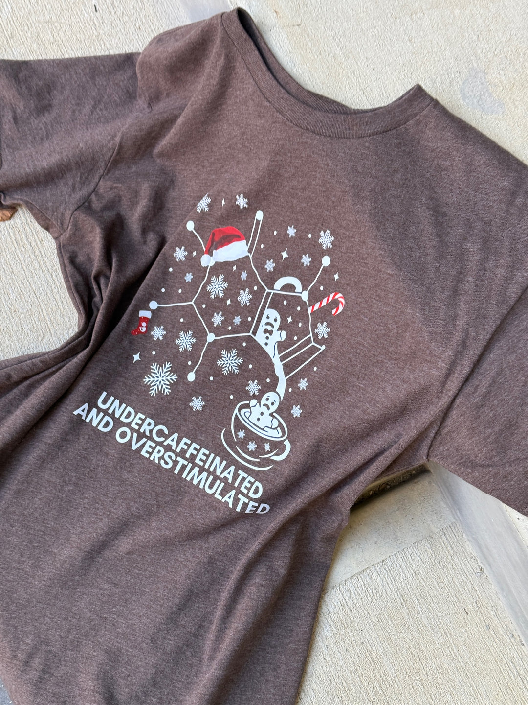 Brown t-shirt with a caffeine molecule Christmas design and 'undercaffeinated and overstimulated' text on a light background