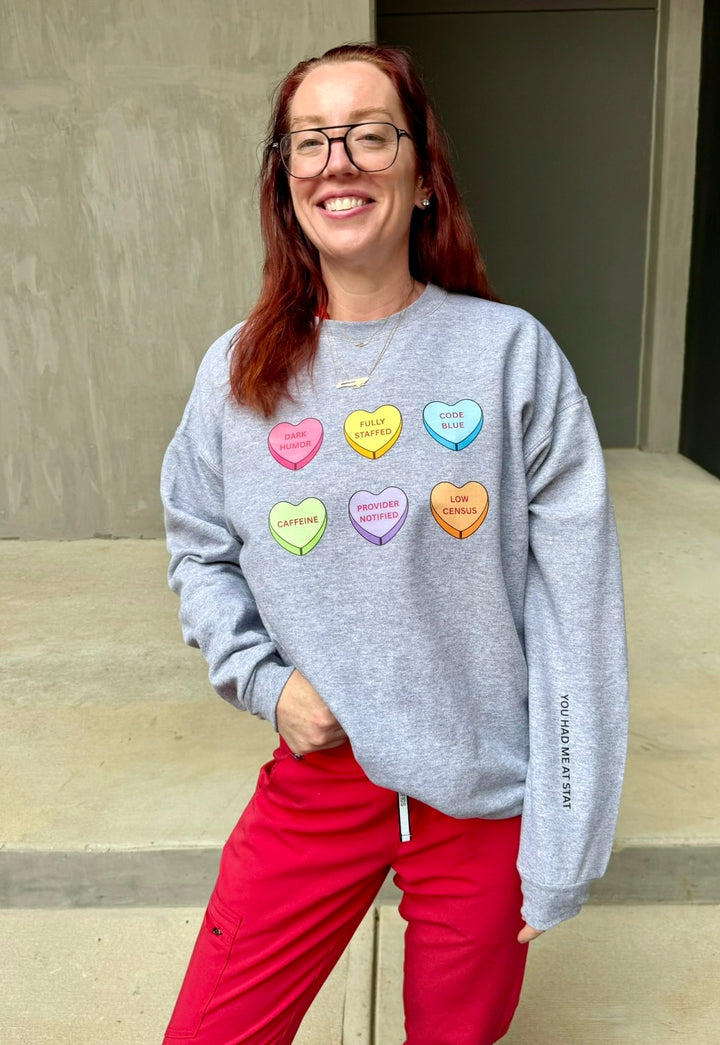 Ladyspinedoc wearing a gray sweatshirt with colorful heart-shaped candy designs and red pants.