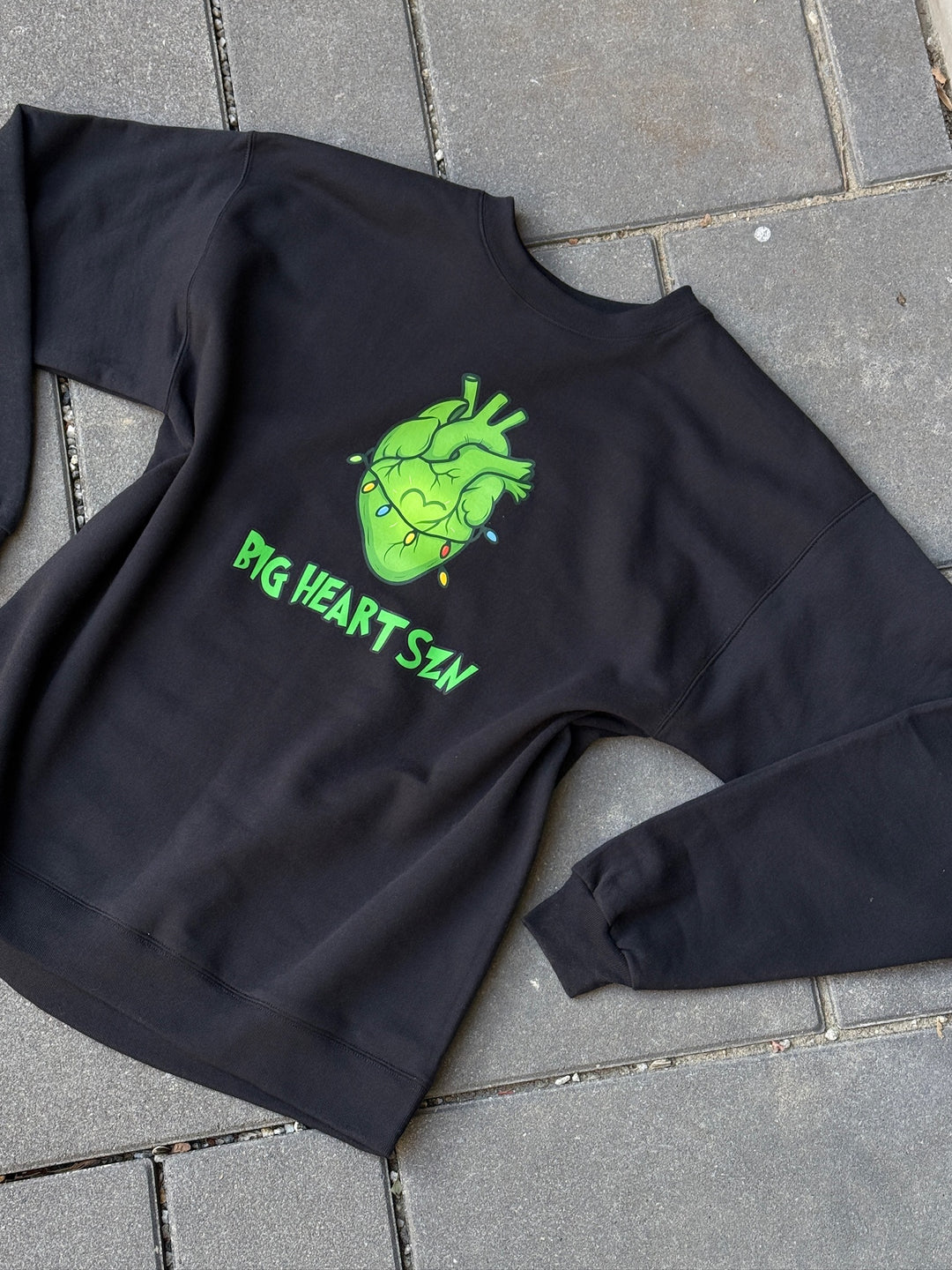 Black sweatshirt with a green heart design and text on a gray pavement background