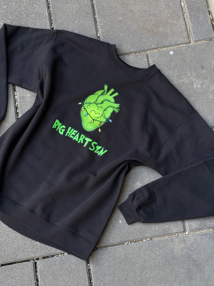 Black sweatshirt with a green heart design and text on a gray pavement background