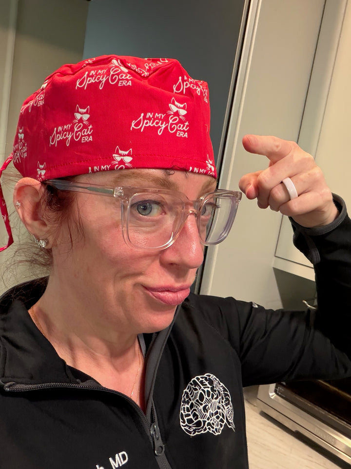 Ladyspinedoc wearing a red scrub cap with In My Spice Cat Era text and clear glasses