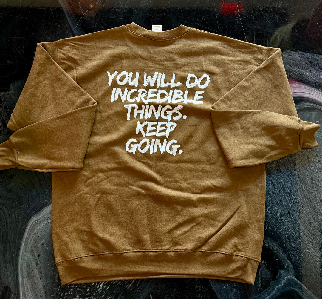 Back of brown-colored Incredible sweatshirt with motivational text on a dark textured surface