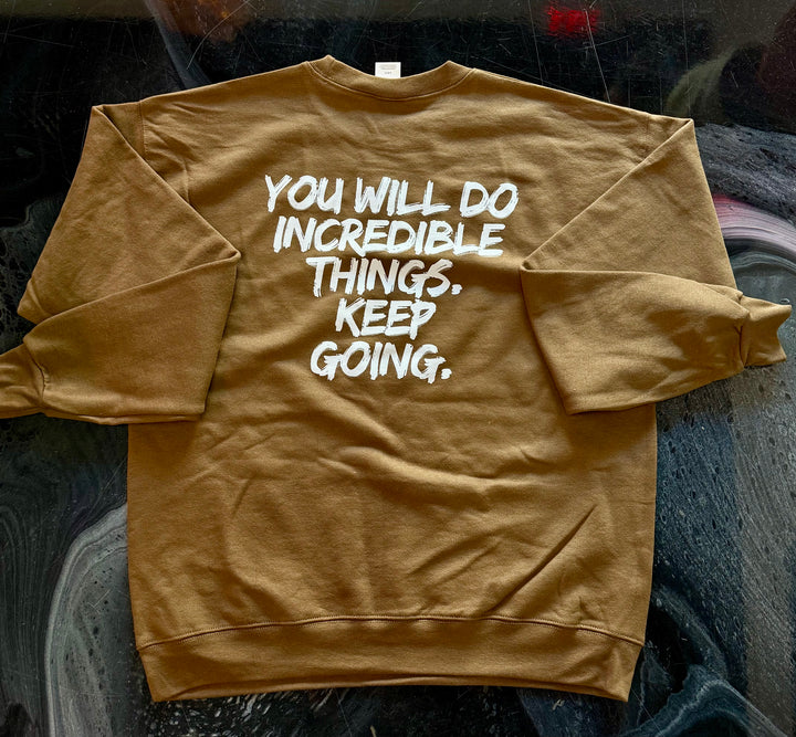 Back of brown-colored Incredible sweatshirt with motivational text on a dark textured surface