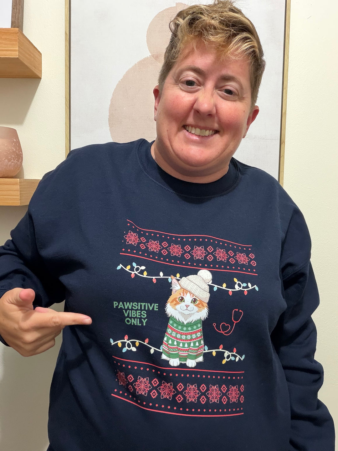 Dr. Beachgem wearing a navy blue Pawsitive Vibes Only Cat Christmas Sweatshirt with a festive design pointing to it.