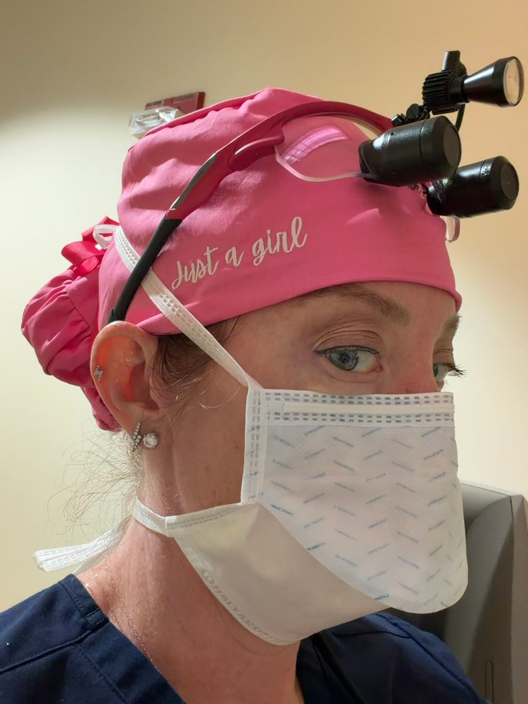 Ladyspinedoc wearing a pink scrub cap with 'Just a girl' text and a surgical mask, in a medical setting.