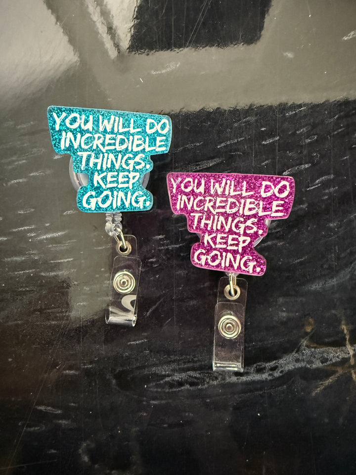 Two "You Will Do Incredible Things. Keep Going." motivational badge reel holders on a dark surface