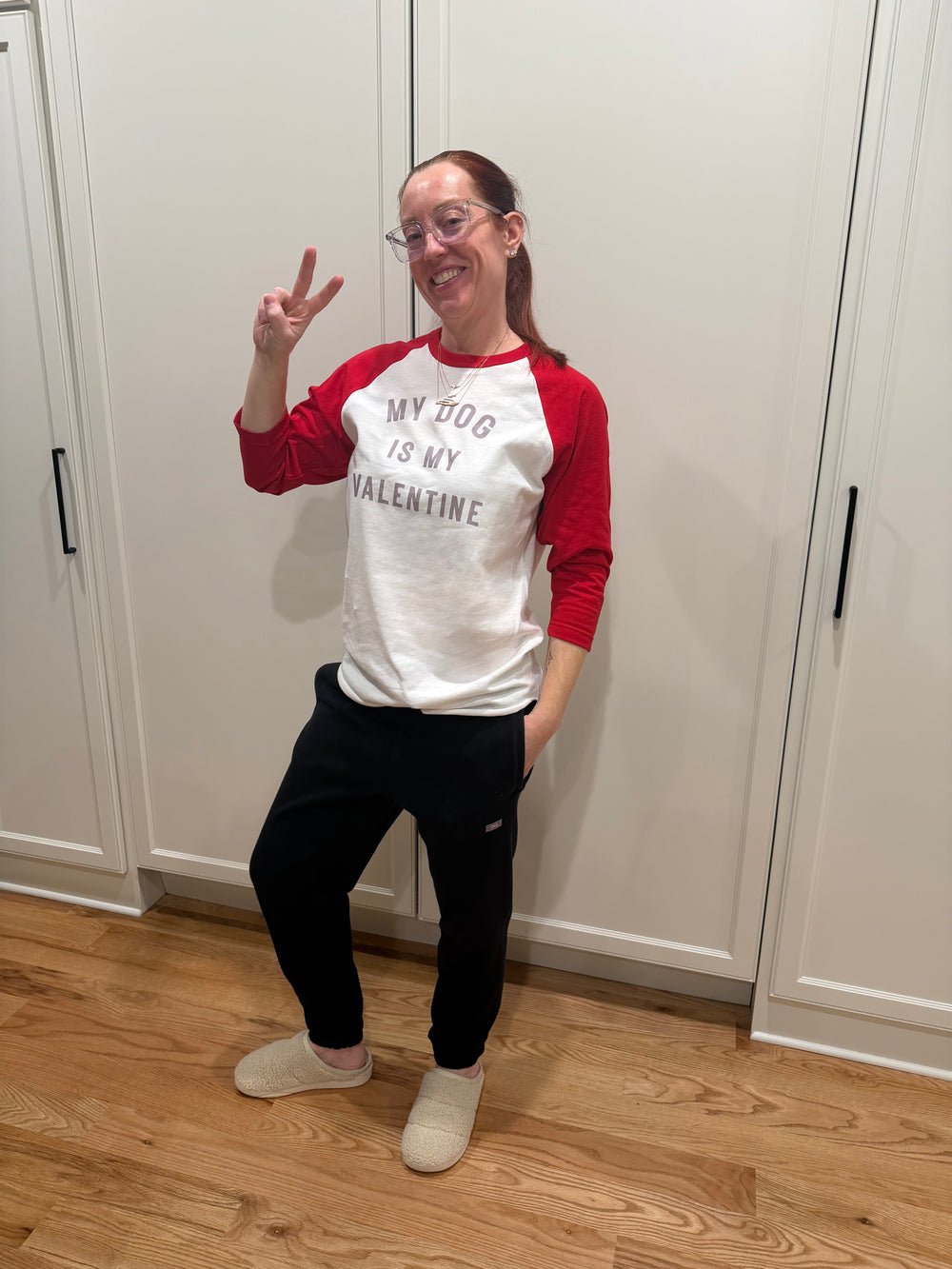 Ladyspinedoc wearing a red and white raglan tee with My Dog Is My Valentine text, standing in a room with wooden floor and white walls.