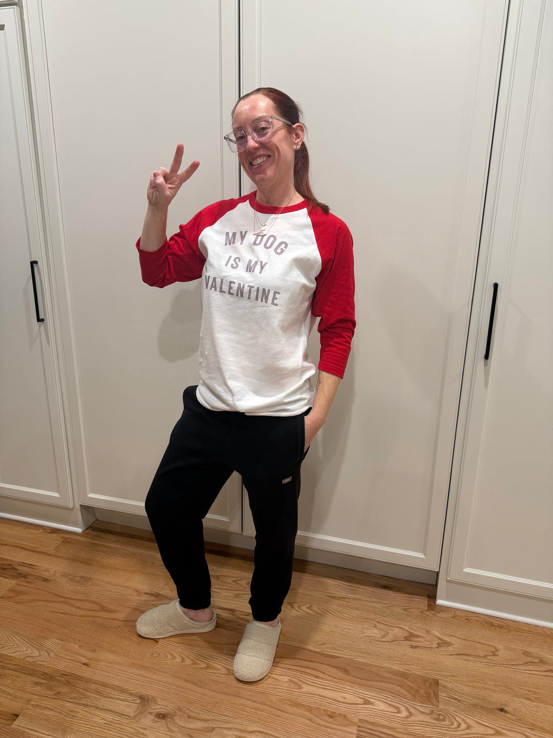 Ladyspinedoc wearing a red and white raglan tee with My Dog Is My Valentine text, standing in a room with wooden floor and white walls.