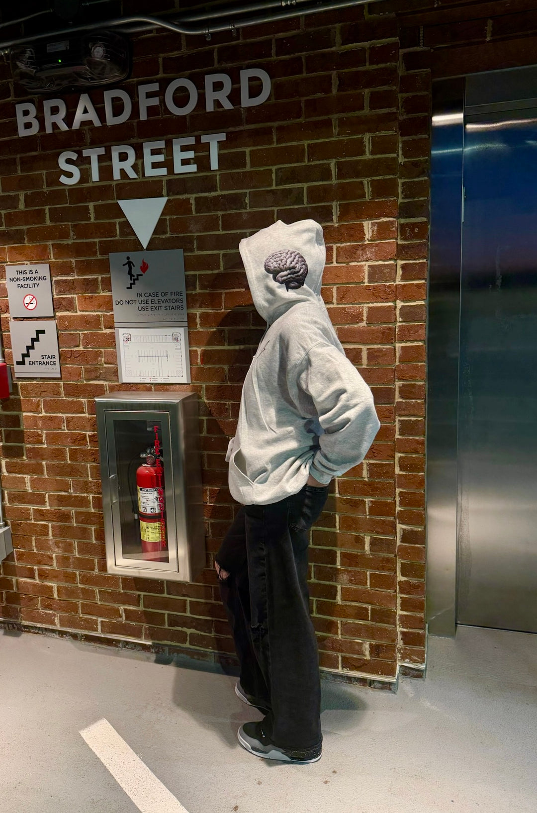 Dr. Betsy Grunch - Ladyspinedoc wearing a light gray hoodie with the hood up, showcasing the brain design on the left side of the hood.
