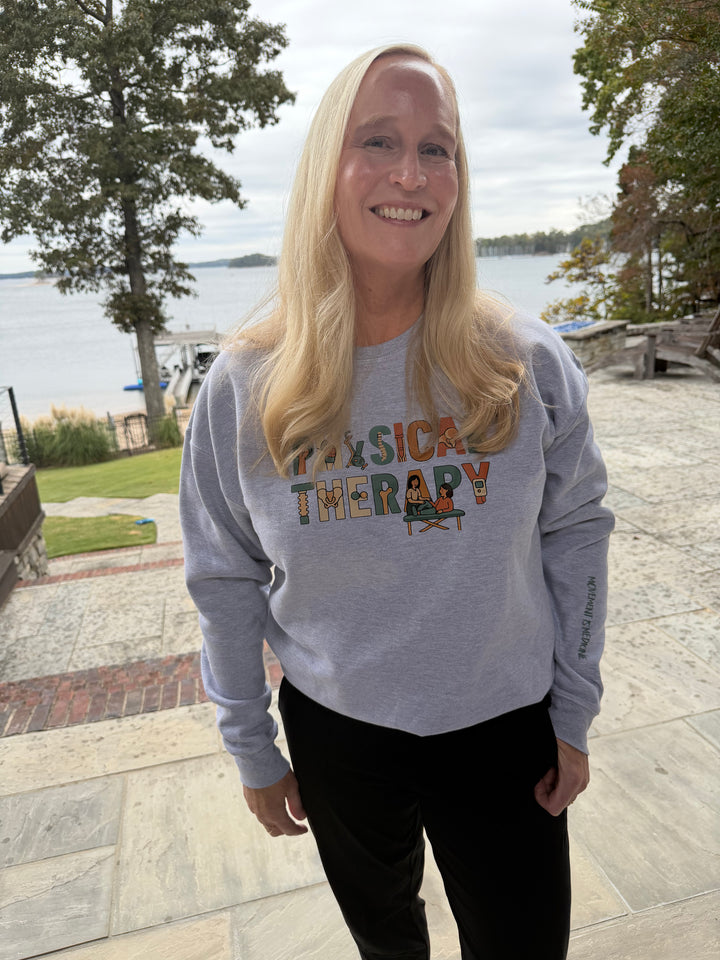 Woman wearing a 'Physical Therapy' sweatshirt by a lakeside.