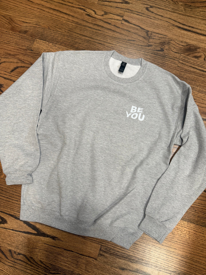 Ash gray sweatshirt with 'BE YOU' text on a wooden surface