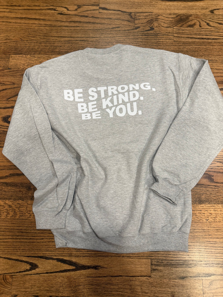Ash gray Be You sweatshirt with motivational text on a wooden surface