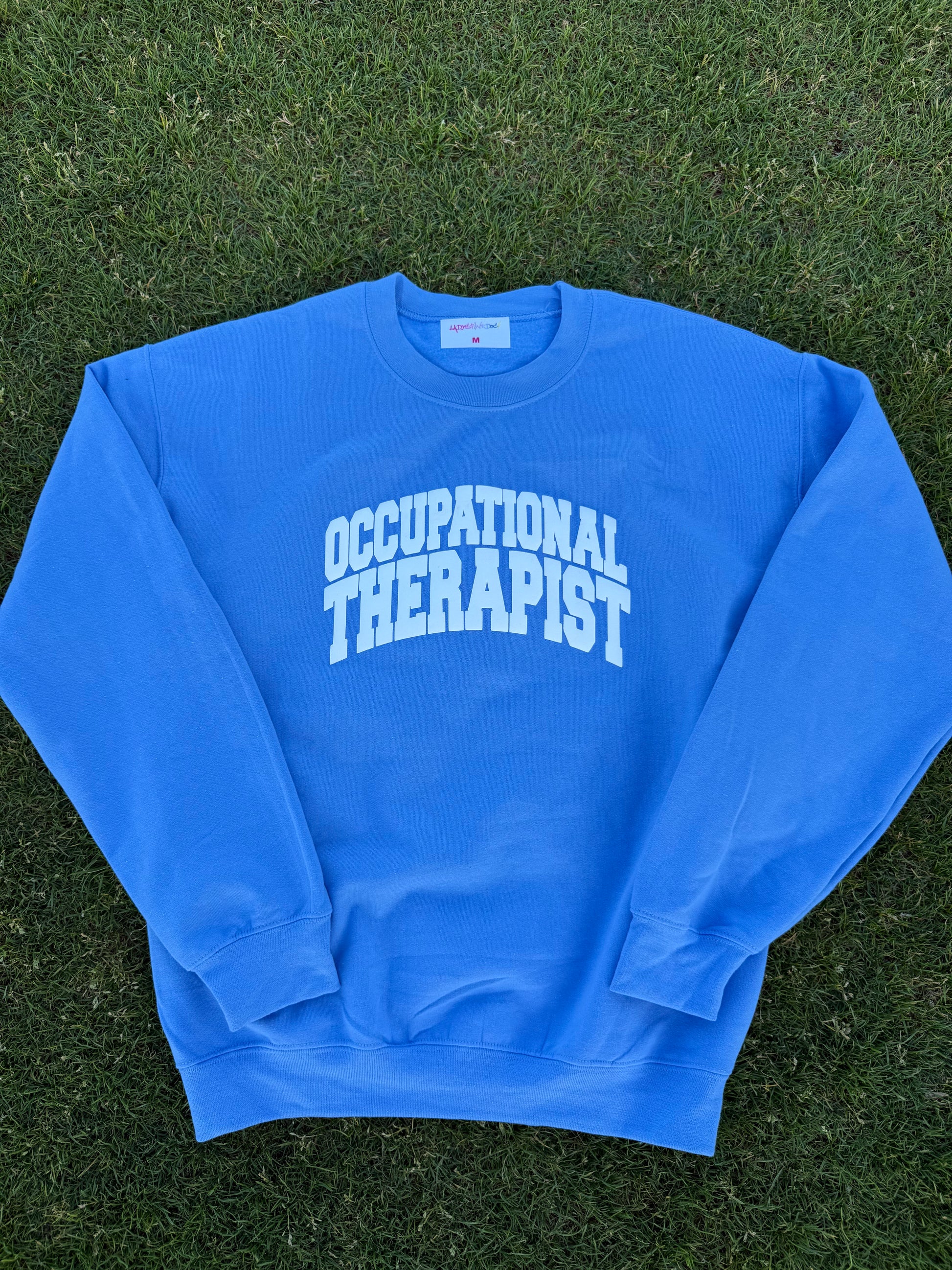 Flat lay of the blue Occupational Therapist crewneck sweatshirt designed by Ladyspinedoc (Dr. Betsy Grunch)