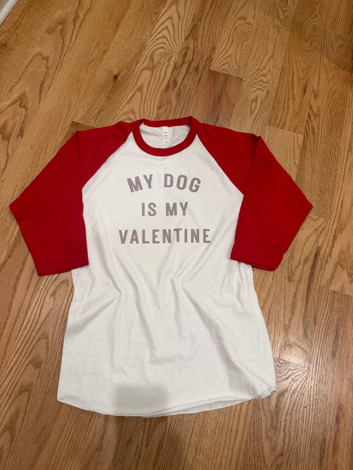 White and red baseball shirt with 'My dog is my valentine' text on a wooden floor.