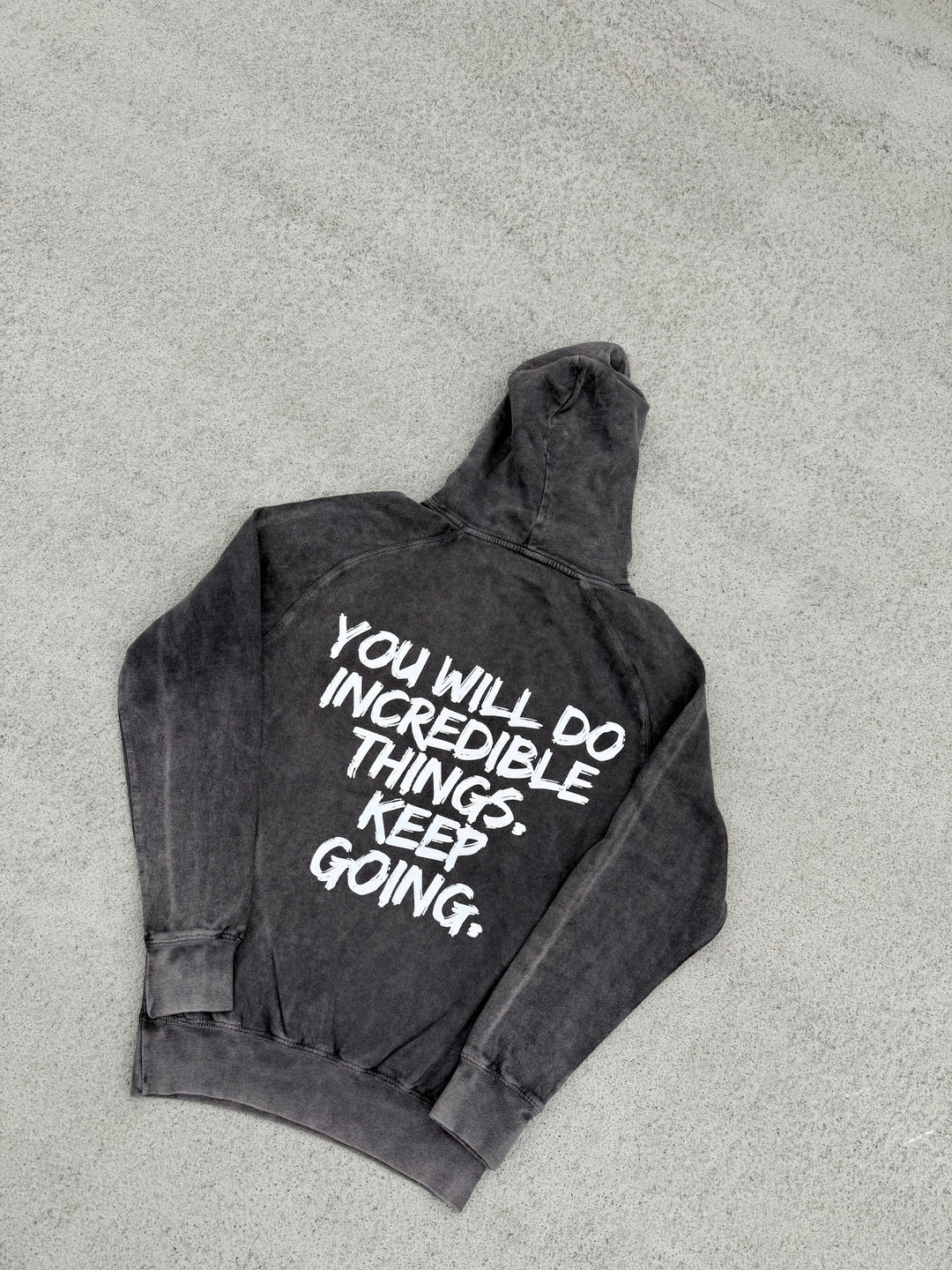Back flat lay of the dark gray Incredible Hoodie with bold white brushstroke message: "YOU WILL DO INCREDIBLE THINGS. KEEP GOING."
