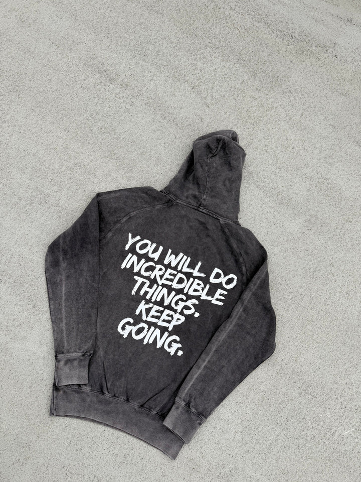 Back flat lay of the dark gray Incredible Hoodie with bold white brushstroke message: "YOU WILL DO INCREDIBLE THINGS. KEEP GOING."
