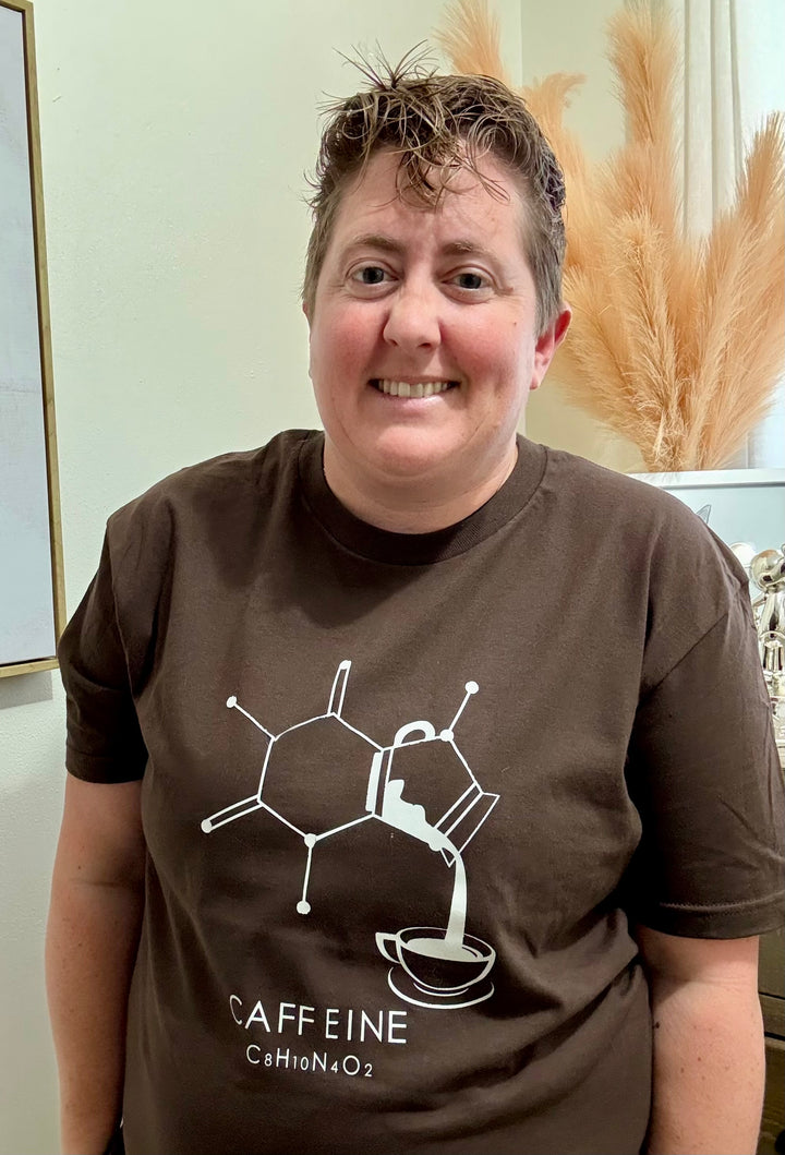 Dr. Beachgem wearing a brown Enerjava t-shirt with a white caffeine molecule graphic, standing indoors.
