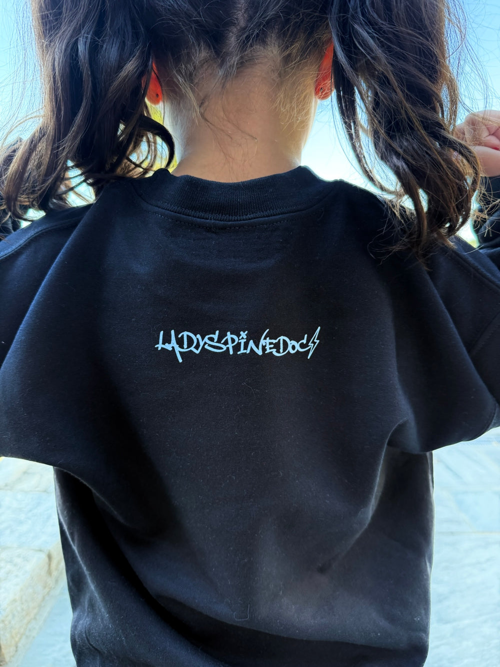 Young girl showing the back of the Super Skull Youth Crewneck Sweatshirt 