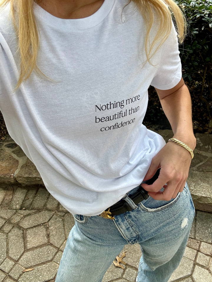 Model outside wearing a white Confidence Tee Shirt that says "Nothing more beautiful than confidence"