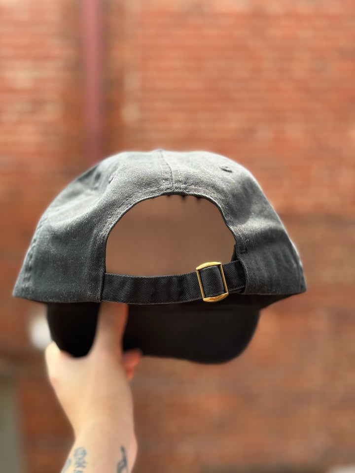 Black cotton strapback ball cap with brass buckle closure, part of the Ladyspinedoc x Confidence Doc collaboration.
