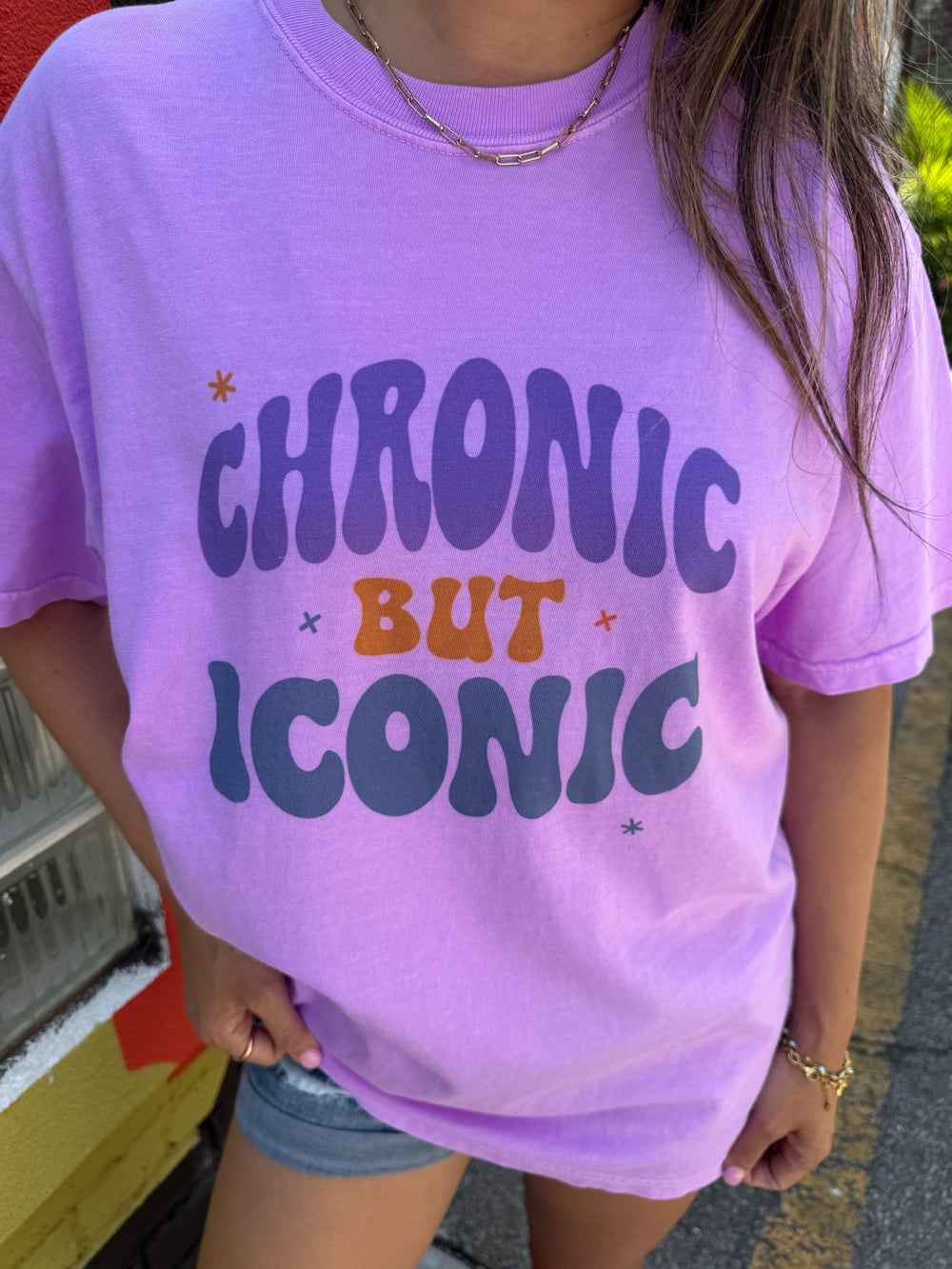 Person wearing a purple t-shirt with 'Chronic But Iconic' text.