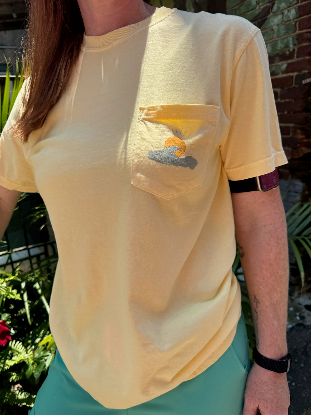 Ladyspinedoc wearing a yellow t-shirt with a pocket design of ocean wave and sun outdoors