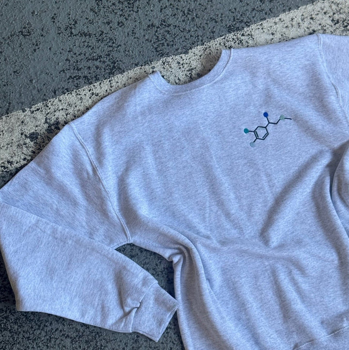 Flat lay on pavement of Ladyspinedoc x Dr. Beachgem Code Cart Crewneck Sweatshirt - Gray Shirt with Embroidered Epinephrine (Adrenaline) Molecule Design