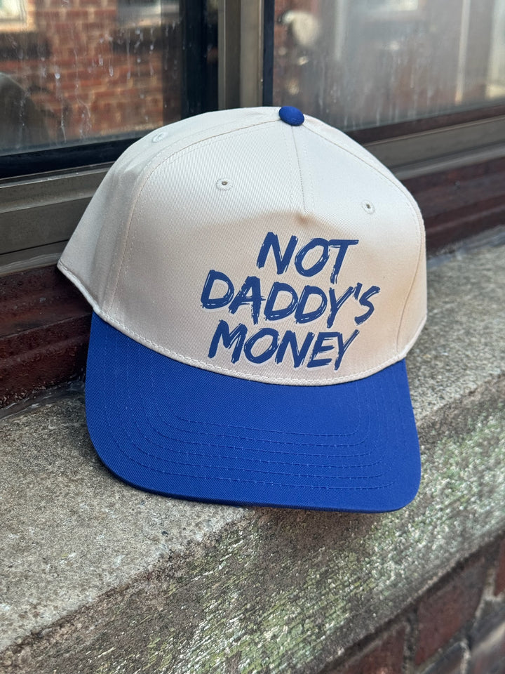 Beige and navy blue cap with 'Not Daddy's Money' text on a stone surface.