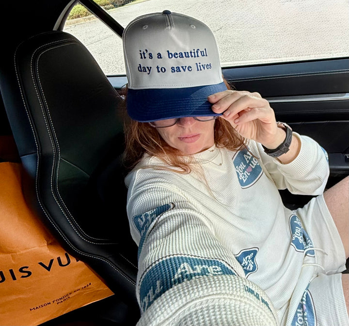 Ladyspinedoc wearing a "it's a beautiful day to save lives" blue and white ball cap while sitting inside a vehicle