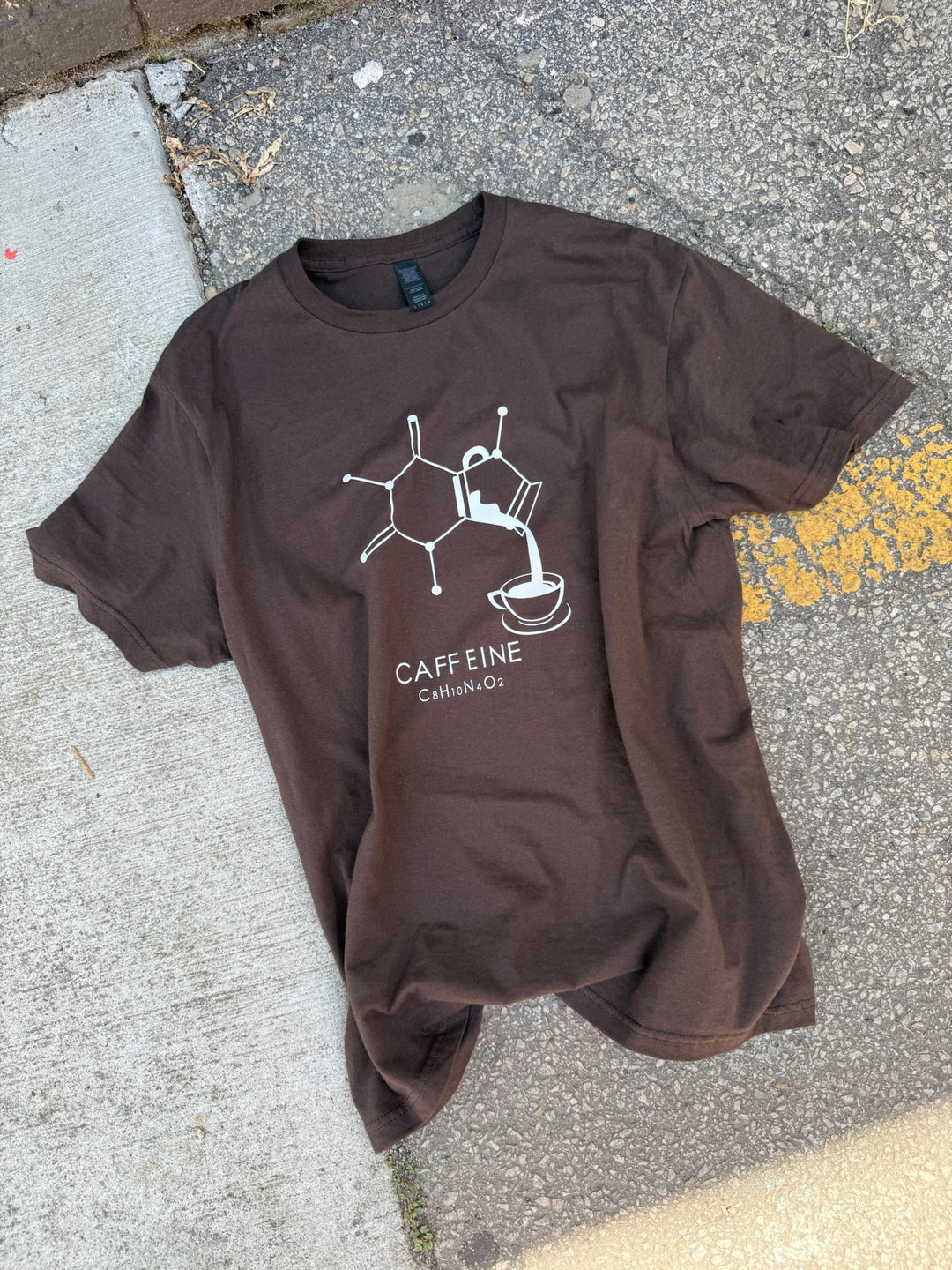 Flat lay of brown Enerjava t-shirt with a graphic caffeine molecule design on a concrete surface