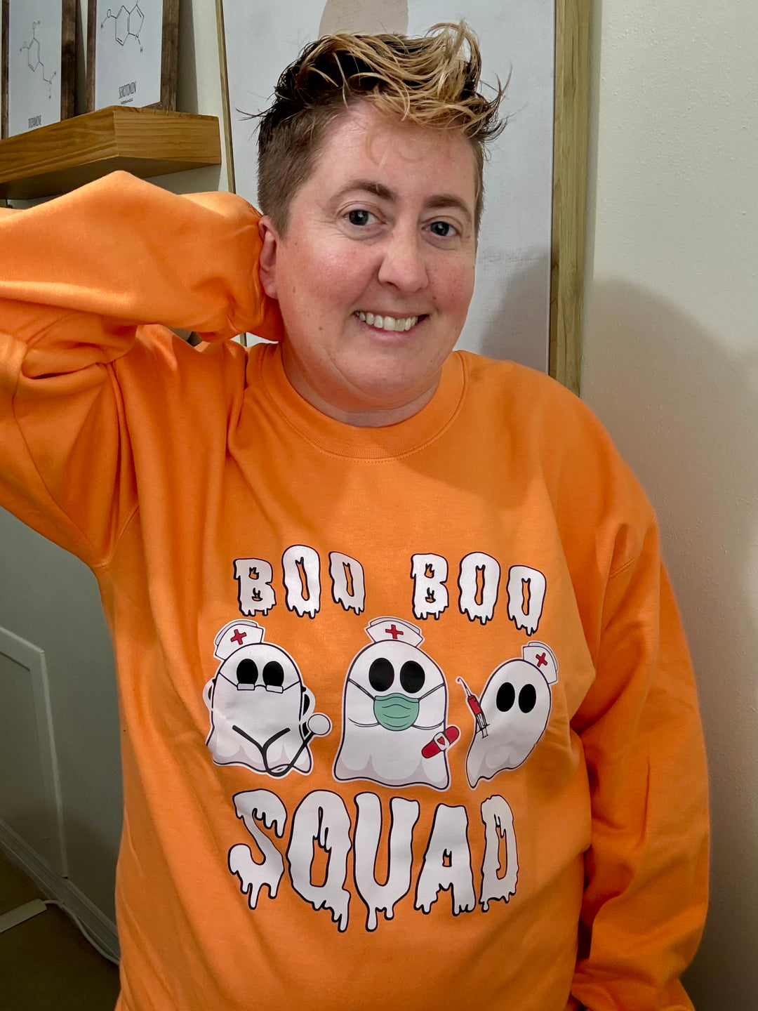 Dr. Beachgem with arm up wearing the orange Boo Boo Squad Crewneck Sweatshirt with ghost nurses